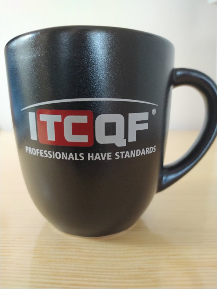 Kubek z logo ITCQF. Hasło poniżej logo głosi &quot;Professionals have standards&quot;.